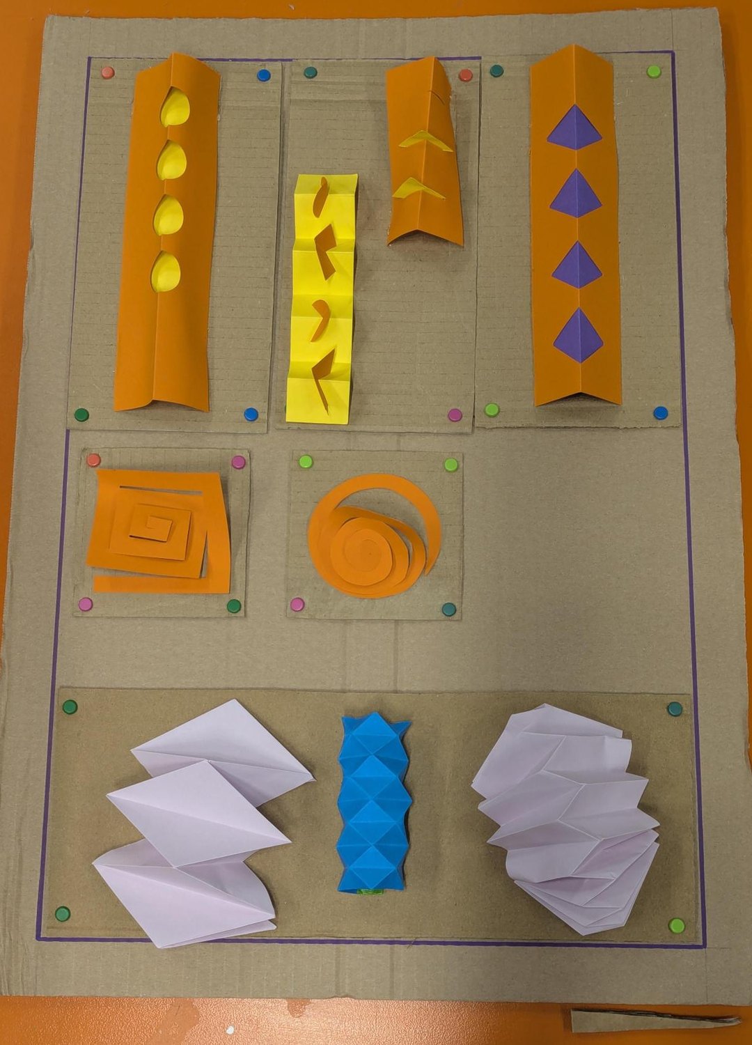 The second board: scored and folded strips in orange and yellow, a cut spiral and a rolled spiral, and three concertina and pleated forms in white and blue.