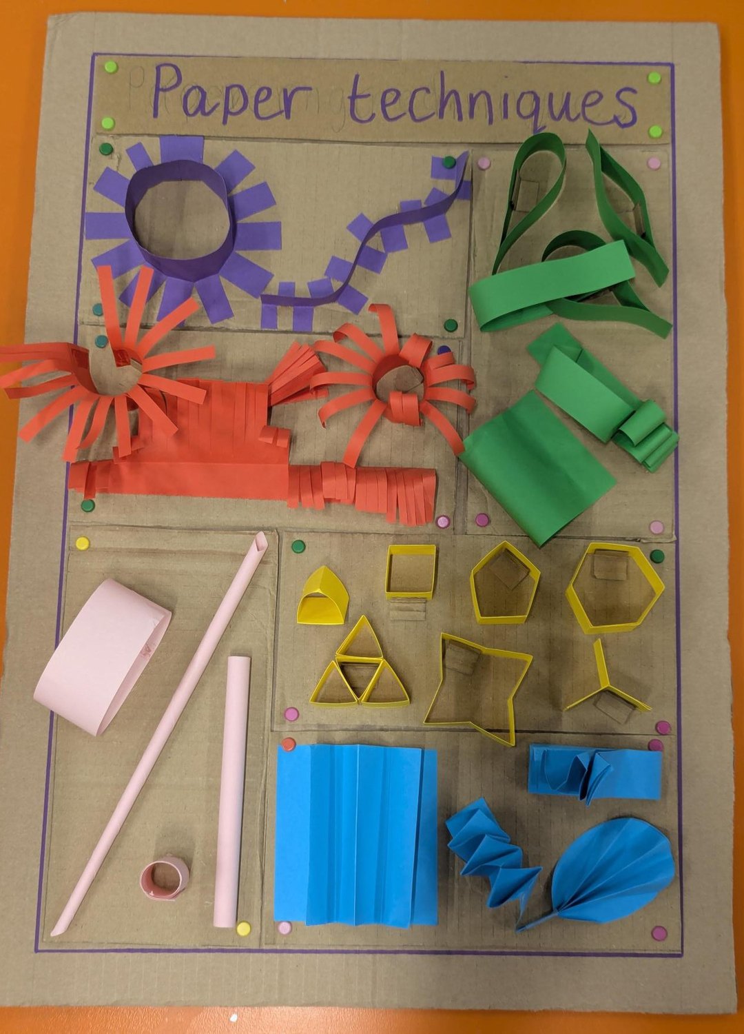 The Paper techniques board: curls and loops in green, a fringed strip and quilled rosettes in red and purple, folded shapes in yellow, pleats and a fan in blue, and rolled tubes.
